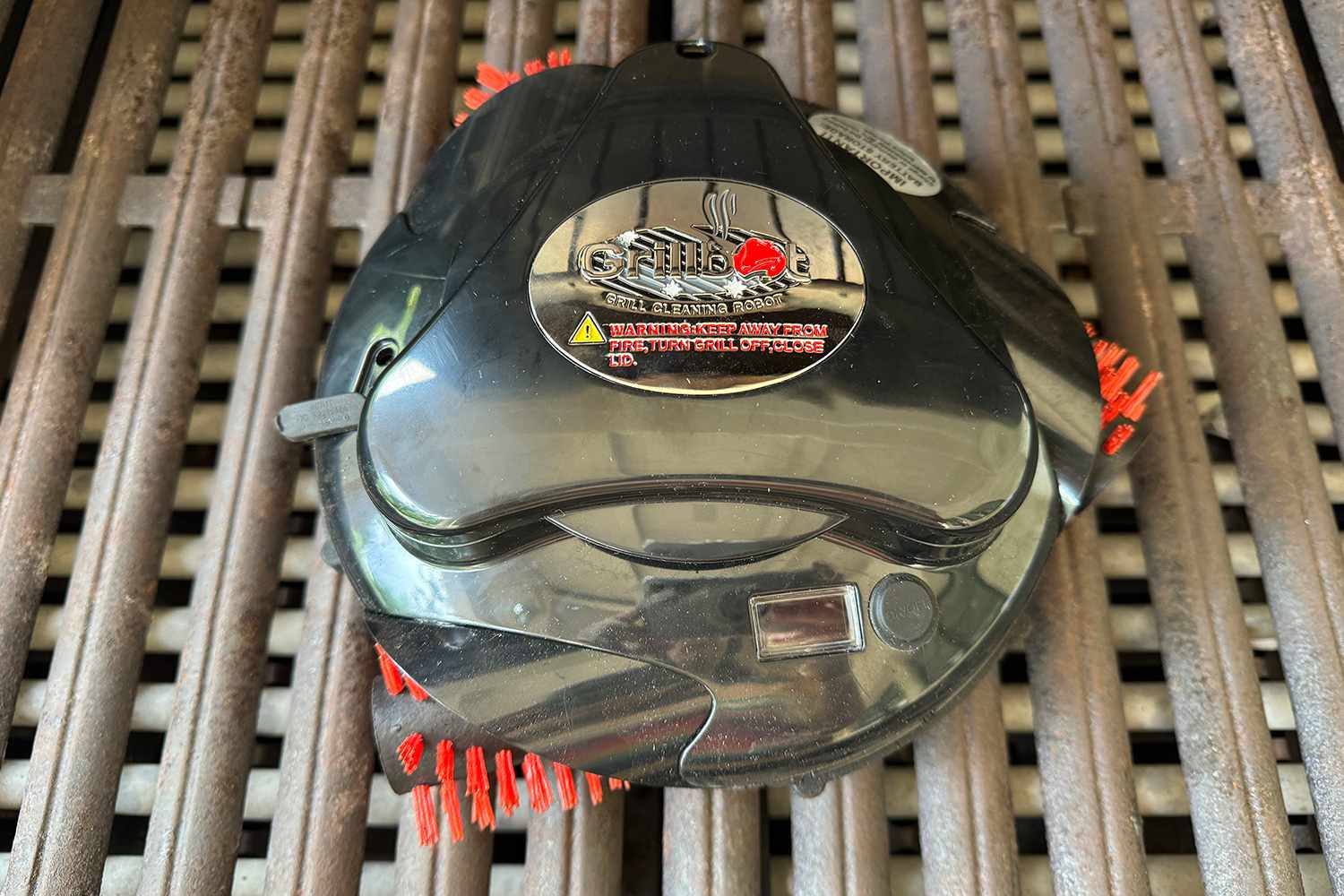 Robotic grill cleaner working on outdoor barbecue grates demonstrating automated scrubbing motion