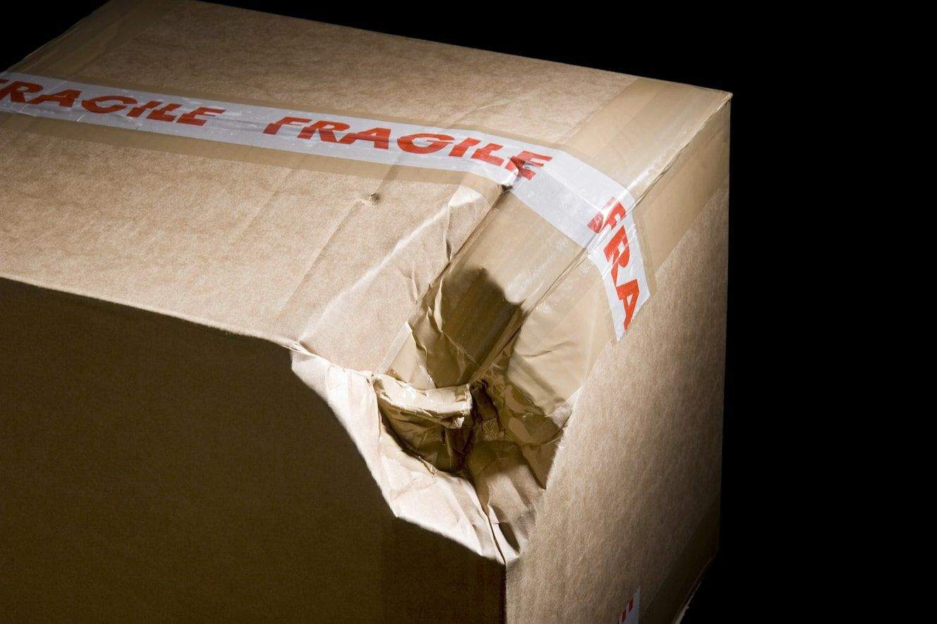 Damaged shipping package arriving at doorstep with crushed corners and torn cardboard